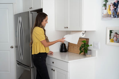 Woman in a kitchen using one hand to tear paper towel from silver paper towel holder
