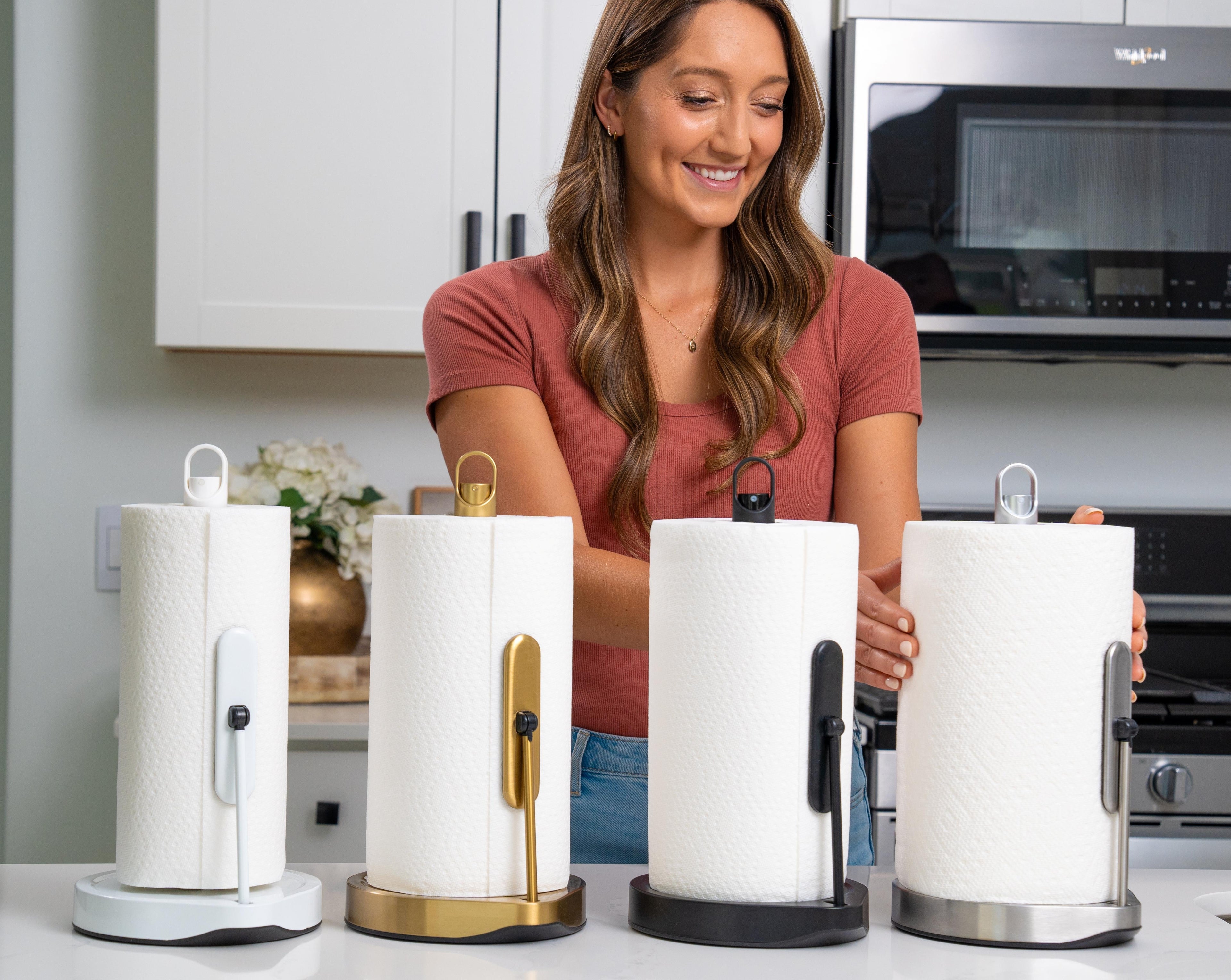 Woman holding four different paper towel holders with paper towels on a kitchen counter.